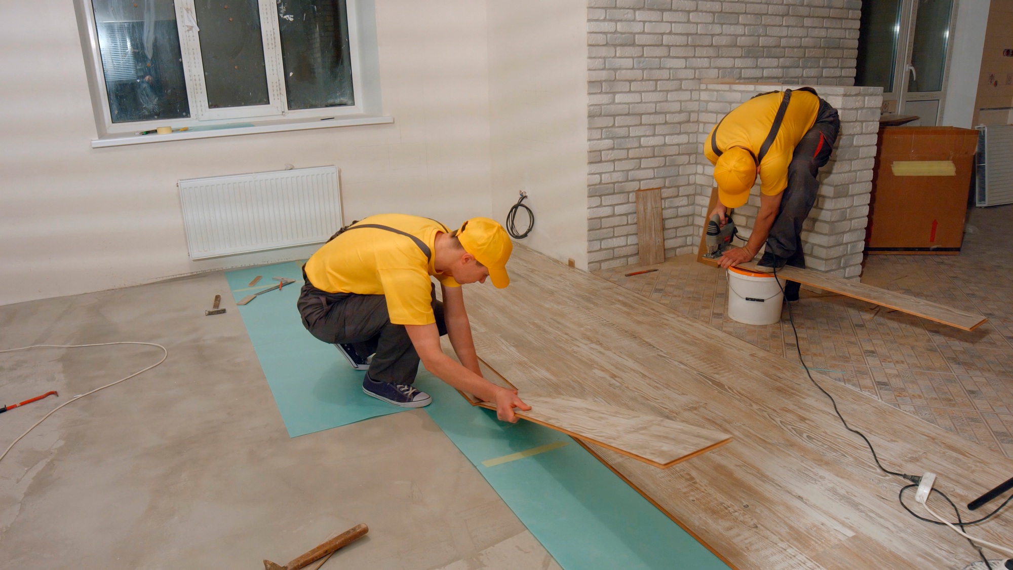 Workers lay laminate flooring in a new home.